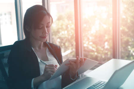 Asian business woman is writing idea down on to a notebook in office workplace.の写真素材