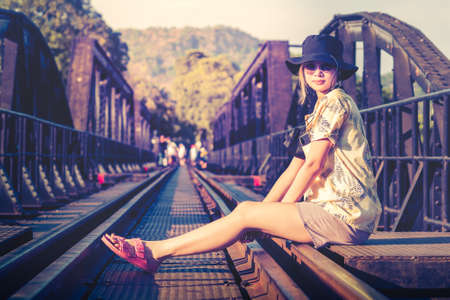 Female Asian tourist is sitting on the old train track of River Kwai Historical site in Kanchanaburi, Thailand.の写真素材