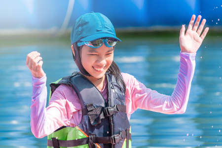 Asian girl is smiling while having fun in a water park with full swim suit and safety on.の写真素材