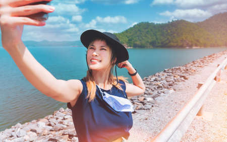 Asian woman in summer dresses is taking selfie using mobile phone on a beautiful beach.の写真素材