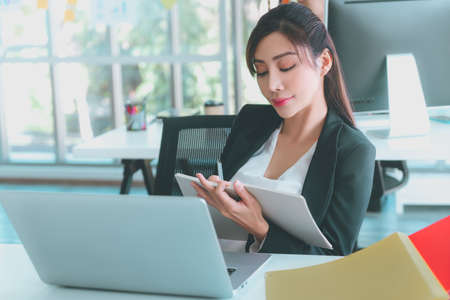 Asian business woman is writing idea down on to a notebook in office workplace.の写真素材