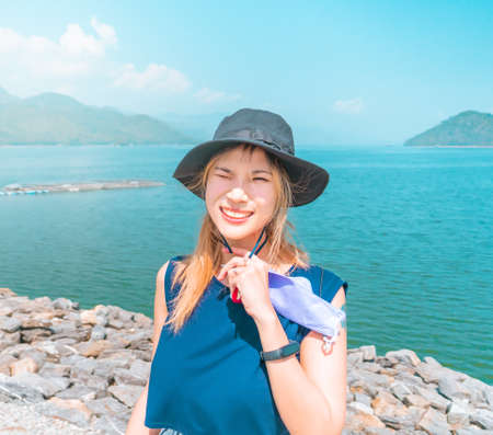 Asian woman with hat and summer wear is taking portrait while on vacation at the beach.の写真素材