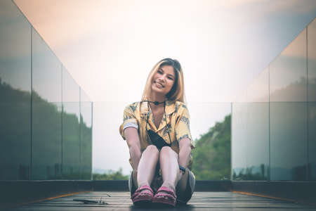 Asian Woman is sitting on wooden glass balcony with nature backgroundの写真素材