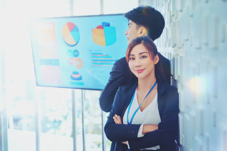 Asian Business Couple male and female standing together for portrait photo in a meeting room with monitor in the background.の写真素材