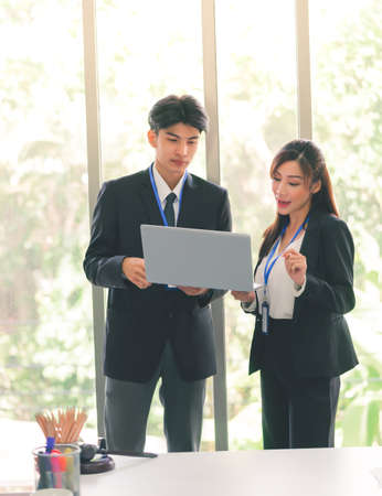 Businesspeople couple male and female standing together disccusing on laptop for teamwork and confident concept.の写真素材