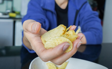 Woman using her hand to pick up potato chips from a bowl, closed up shot.の写真素材