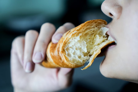 Woman eating a croissant in her hand, closed up shot.の写真素材