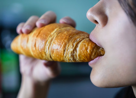 Woman eating a croissant in her hand, closed up shot.の写真素材