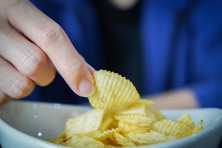 Woman using her hand to pick up potato chips from a bowl, closed up shot.の写真素材
