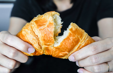 Woman tearing and breaking a croissant in her hand, closed up shot.の写真素材