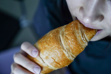 Woman eating a croissant in her hand, closed up shot.