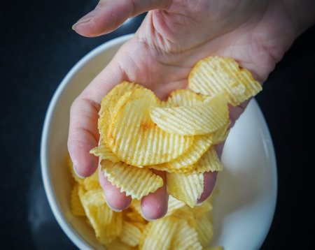 Woman using her hand to pick up potato chips from a bowl, closed up shot.の写真素材