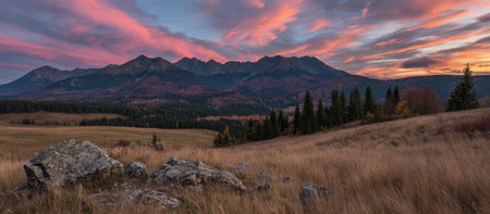 Sunset over mountain range with fiery sky, field, rocks, and trees. Landscapeの素材
