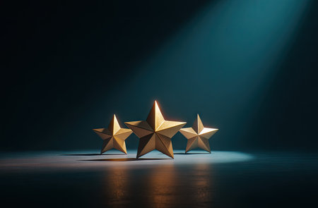 Three golden stars are illuminated by a spotlight on a dark blue backdropの素材