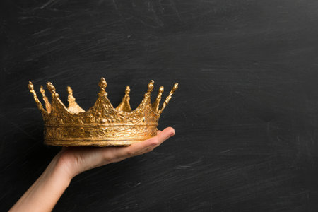 A golden crown rests on a hand against a dark backdrop, emphasizing royalty and powerの素材