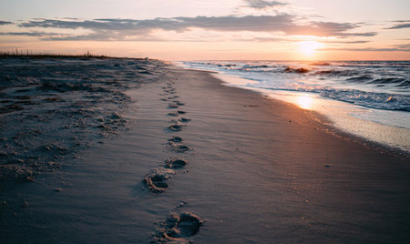 A beach at sunset, footprints in the sand leading to the ocean under a colorful skyの素材