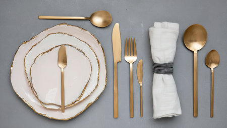 Overhead view of a table setting plates, gold cutlery, and a folded napkin on grayの素材