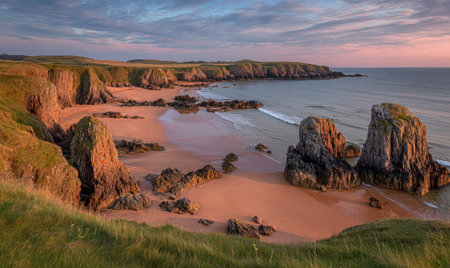 Coastal view featuring sandy beach, towering cliffs, and vibrant sunset hues over the waterの素材
