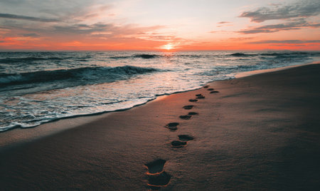 Footprints lead across a beach at sunset, waves gently lap the shoreの素材