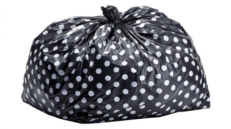 A black trash bag, patterned with white polka dots, is isolated against a clean white backdrop. The glossy surface catches the light, highlighting the texture and pattern. The image suggests a clean environment and can be utilized for various commercial or editorial needs.の素材