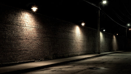 A brick wall is the main focus, lit by multiple overhead streetlights at night. The scene features a dark environment, with a road in front and the wall in the background. The lighting creates dramatic shadows. This image can be used for various design and advertising projects.の素材
