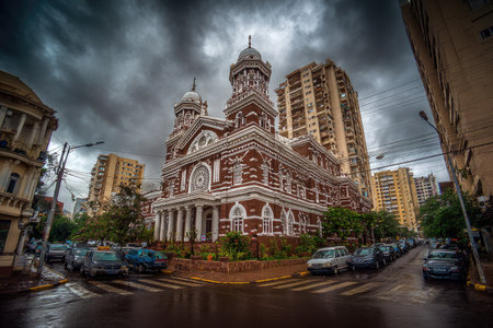 A grand building showcases ornate architecture with intricate brickwork, contrasted by a moody, overcast sky. The image features a composition of buildings, vehicles, and street elements. The lighting enhances the textures and colors, suitable for diverse commercial and editorial applications related to urban development.の素材
