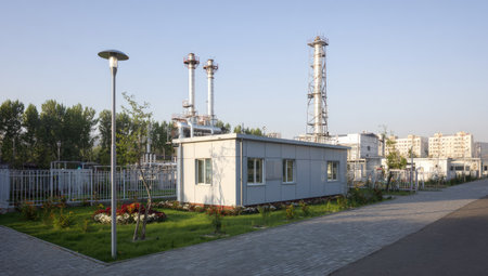 An industrial building features multiple chimneys and a surrounding environment. The composition shows a low-angle view with a paved walkway in the foreground. Soft natural lighting reveals the building's exterior and grassy areas with trees under a clear daytime sky. The image could be used for commercial or editorial purposes.の素材