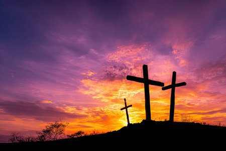 Three dark crosses stand silhouetted atop a hill, set against a vibrant sunset of purples, oranges, and yellows. The composition features a dramatic contrast between the dark foreground and the bright, colorful sky. This image could be used for various editorial and commercial applications.の素材
