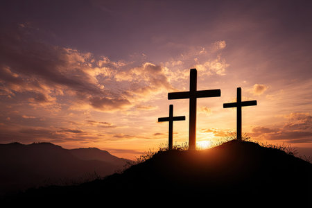 Three dark crosses stand silhouetted against a vibrant sunset sky. The warm, golden light contrasts with the dark forms. The composition includes rolling hills and clouds, suggesting an outdoor setting. This image could be suitable for editorial content and religious themes.の素材