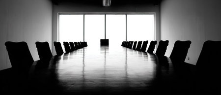 An empty conference room is depicted in a monochromatic composition. A long table dominates the scene, flanked by rows of chairs. The natural light pours through large windows, illuminating the space. This image is suitable for various commercial or editorial uses such as business, corporate, or office-related themes.の素材