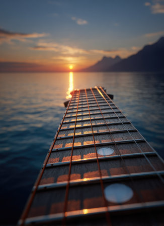A guitar neck is the central subject, set against the backdrop of a body of water and setting sun. The composition features warm hues reflecting across the water's surface. The image portrays a natural environment at dusk. This visual is suitable for artistic, musical, or travel related projects.の素材