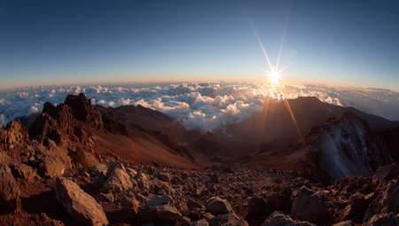 An aerial perspective shows mountain terrain with sunlight breaking through clouds. The warm lighting illuminates the rugged landscape, creating a dramatic contrast. This image, likely shot at dawn or dusk, evokes a sense of vastness and natural beauty and could be used for travel, landscape, or environmental projects.の素材