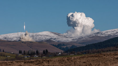 A rocket ascends from a launch site, leaving a trail of smoke against a backdrop of snow-covered mountains. The scene features a clear blue sky and a large cloud formation near the mountains. The image could be used for illustrating technology, space exploration, or scientific advancements.の素材