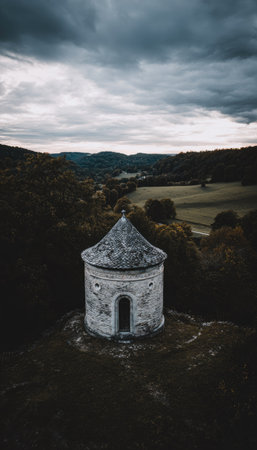 A stone structure with a conical roof stands prominently on a hillside. The scene is bathed in cool tones with a dark, moody atmosphere, featuring a cloudy sky and surrounding forest. The image's composition and color palette are suitable for commercial and editorial applications.の素材