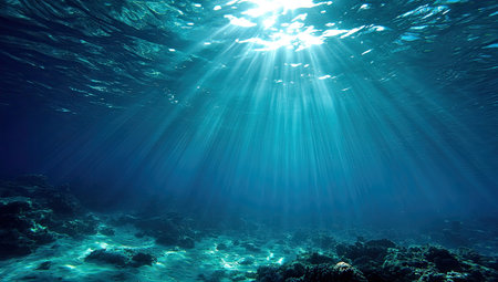 The image showcases an underwater view with sunbeams penetrating the water's surface. A dark blue hue dominates, accented by the bright sunlight creating an ethereal ambiance. The composition is natural with soft textures and lighting creating a serene setting. This image could be used for various design projects or editorial purposes.の素材