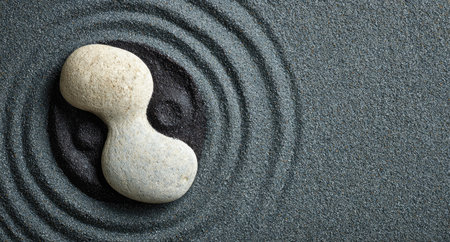 A smooth, light-colored stone rests on a dark gray sand surface meticulously raked into circular patterns. The composition features contrasting textures and colors, with soft lighting emphasizing the serene atmosphere. This image could be used for projects related to relaxation, meditation, or conceptual design.の素材