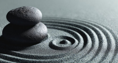 Two stones are stacked in balance, centered in a circular sand pattern. The monochromatic palette of gray and white creates a minimalist aesthetic. The composition utilizes shallow depth of field. This image may be suitable for wellness publications, relaxation themes, or abstract art.の素材