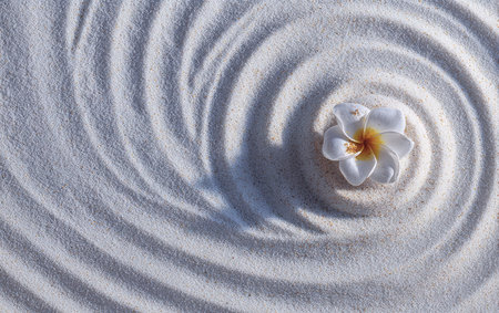 An overhead view reveals a white flower at the center of carefully raked sand spirals. The image highlights texture and pattern, the circles forming a peaceful composition. This tranquil scene suggests themes of meditation and well-being, suitable for various design and editorial projects.の素材