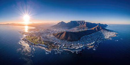 A panoramic view displays a mountain range surrounded by water under a clear sky. The composition features a wide-angle perspective, showcasing the natural landscape. The lighting is bright, with the sun visible, suggesting daytime. This image would be suitable for travel brochures or editorial content.の素材