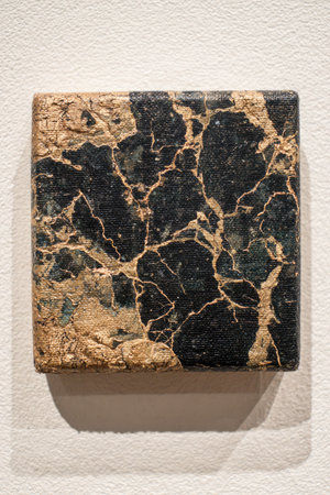 A square art piece displays a dark color scheme with gold-colored veins and accents. The artwork is set against a plain white background. Its textured surface creates shadows. This image may be suitable for various commercial or editorial applications, providing a unique visual element for different projects.の素材