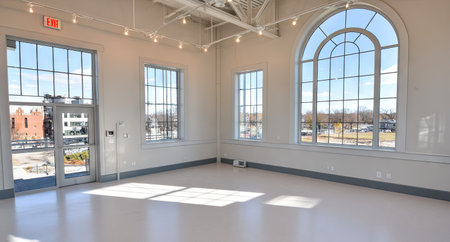 An empty, brightly lit room features expansive windows offering outdoor views. The interior showcases clean white walls and a reflective floor. Overhead lighting accents the open space. The image is suitable for various commercial applications emphasizing space and design.の素材