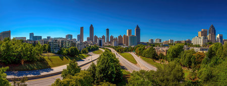 This panoramic view depicts a vibrant cityscape featuring numerous skyscrapers dominating the skyline. The scene is set under a bright blue sky, with roads and lush green trees in the foreground. This image may be suitable for various commercial applications, including travel, urban development, or architectural themes.の素材