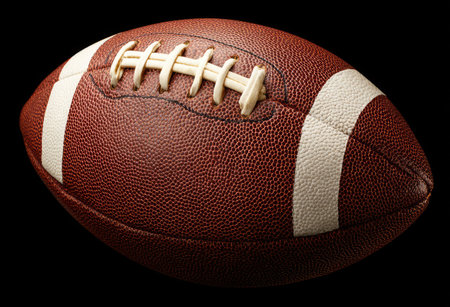 An American football is presented in a close-up shot against a dark background. The ball features a brown leather exterior, detailed stitching, and white stripes. The composition emphasizes the ball's texture and shape. This image could be utilized for sports-related editorials or commercial projects.の素材