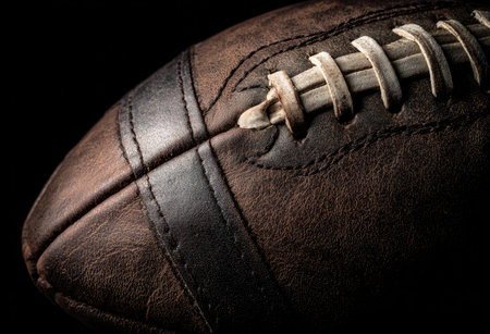 This image presents a detailed close-up of a brown, textured leather American football. The composition features a dark background, highlighting the ball's stitching and surface. The lighting emphasizes the form and depth, suitable for various sports-related projects and commercial applications. It showcases the classic design.の素材