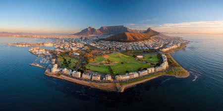 An aerial panoramic view reveals a coastal cityscape with a prominent mountain backdrop. The scene showcases a blend of urban development and natural elements, including water. The composition displays vibrant colors and a clear sky, suggesting a daytime setting. Suitable for travel, architecture, and landscape concepts, the image offers versatile visual potential.の素材