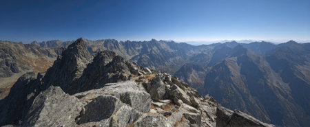 A panoramic photograph showcases a majestic mountain range under a clear blue sky. The foreground features rough, gray rocks with textures, while the distant mountains exhibit a hazy, layered effect. This image would be suitable for various commercial and editorial applications, possibly conveying a sense of grandeur.の素材