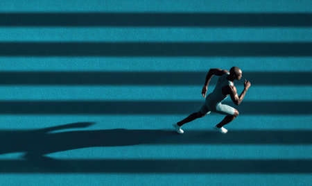An athlete sprints across a blue track with black lines. The composition features an overhead perspective. The colors are predominantly blue and black with shadow. The image conveys speed and athleticism suitable for commercial uses.の素材