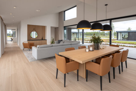 A spacious interior presents a dining table surrounded by chairs. Overhead lighting illuminates the setup. A large window offers a view of an outdoor scene. The composition suggests modern architecture with potential uses in lifestyle publications and real estate marketing materials.の素材