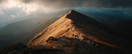 An aerial view presents a mountain peak bathed in warm sunlight, contrasting against a dark, cloudy sky. The composition highlights textures of rock and the atmospheric effect. This image is suited for editorial use and commercial purposes related to nature, adventure, or landscape photography.の素材