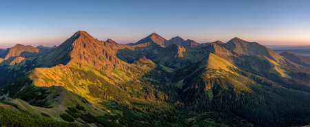 A scenic landscape showcases a majestic mountain range under a clear blue sky. The image reveals detailed textures of the mountains, illuminated by sunlight, casting shadows across the valleys. The natural tones and composition could be used for various commercial and editorial purposes, representing the beauty of the outdoors.の素材